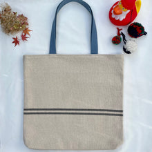 Load image into Gallery viewer, Tote bag. Heavyweight natural woven canvas with two horizontal blue grey stripes. Lined with a beautiful striped cotton shirting fabric.
